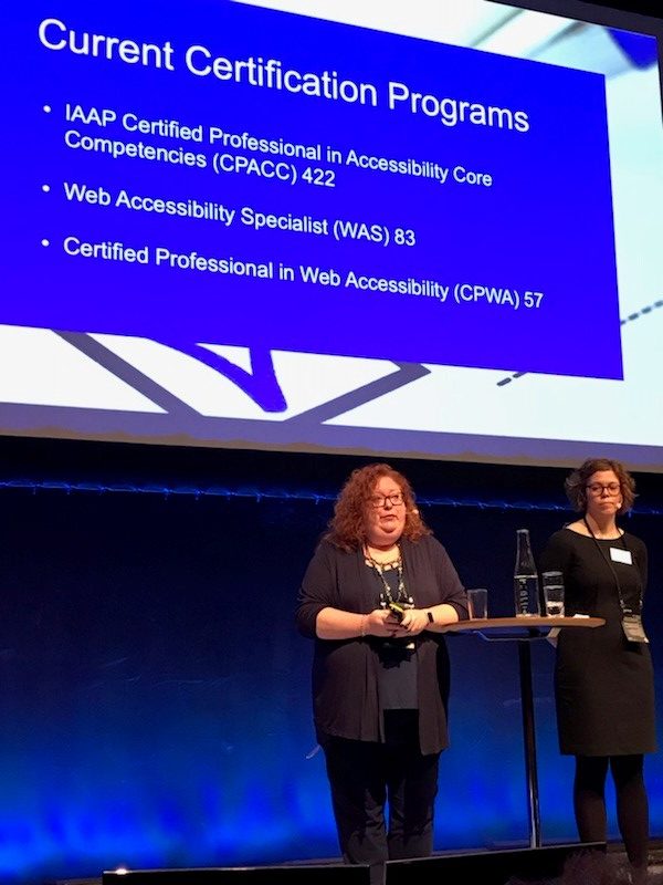 Samantha Evans standing on a stage presenting a slide on IAAP's certification programs.