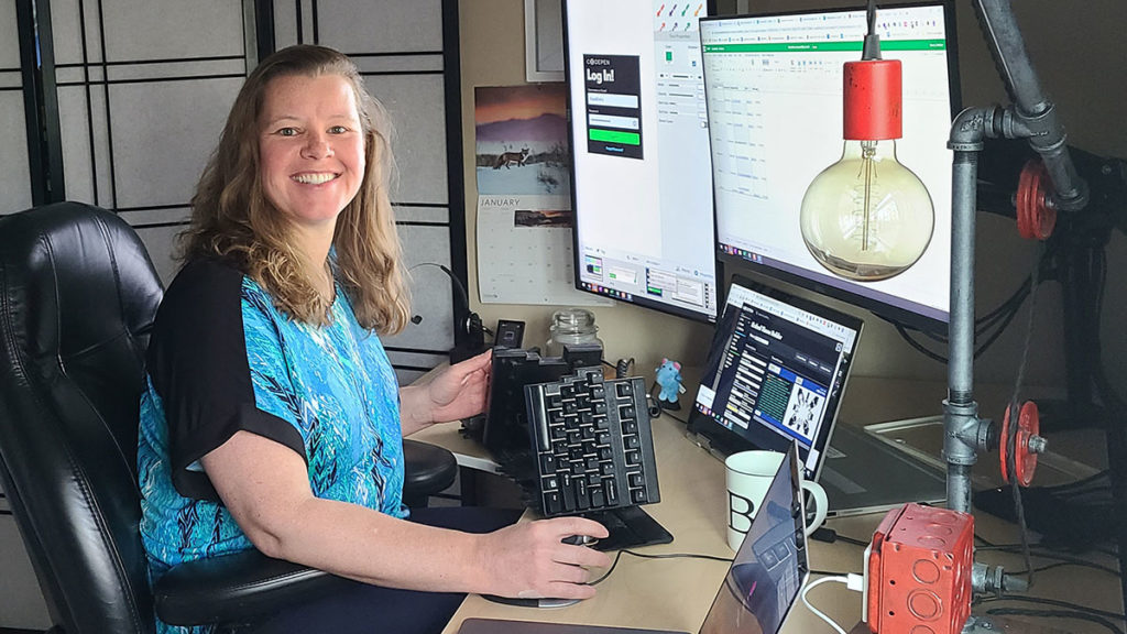 Heather sits in her office in front of three monitors and a split keyboard