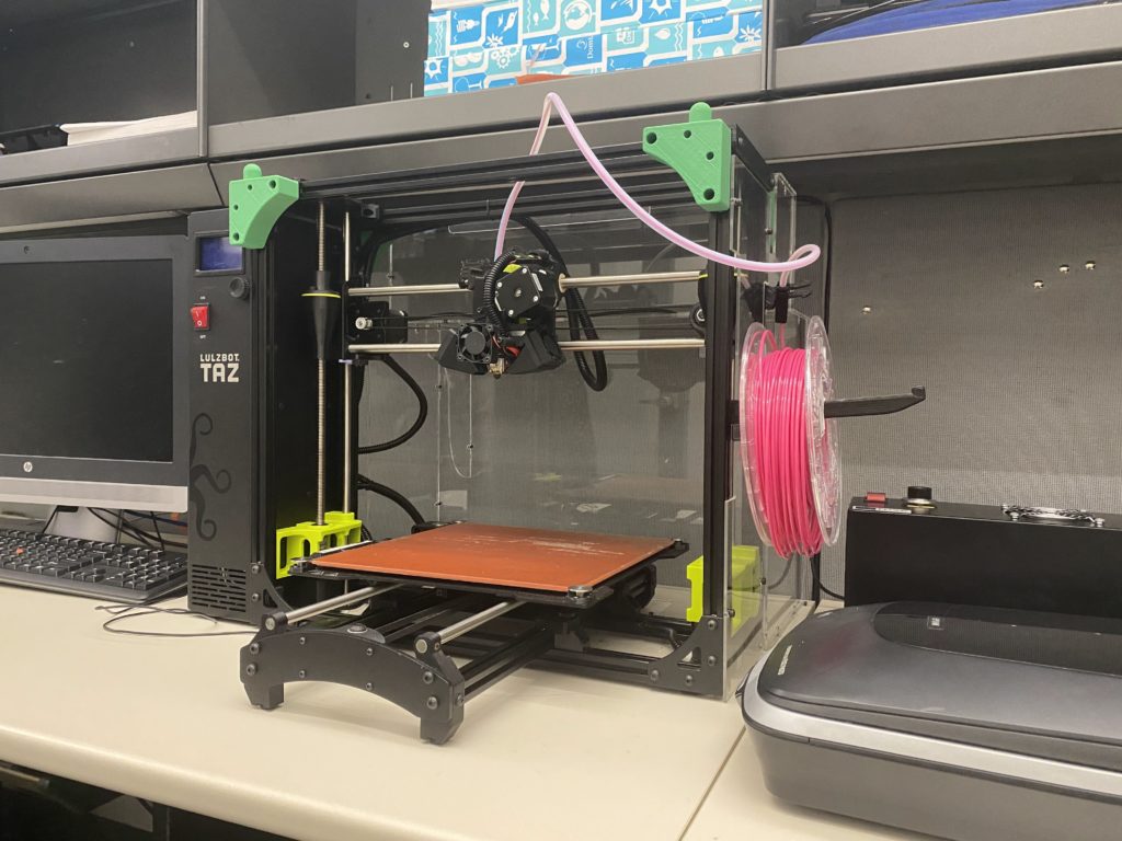 LulzBot TAZ printer with a flat plate, printing contraption above the plate, and pink filament on the side