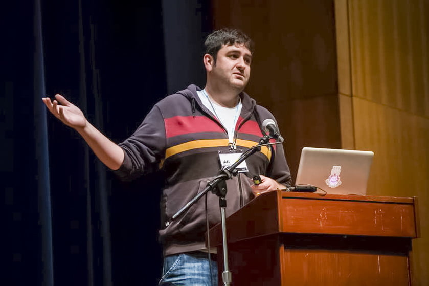 Ian Hamilton stands in front of a podium and a microphone and laptop