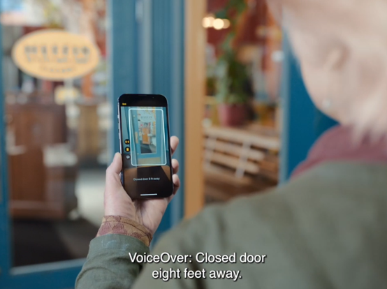 A hand holding an iPhone aims at a door. Captions say "VoiceOver: Closed door eight feet away."